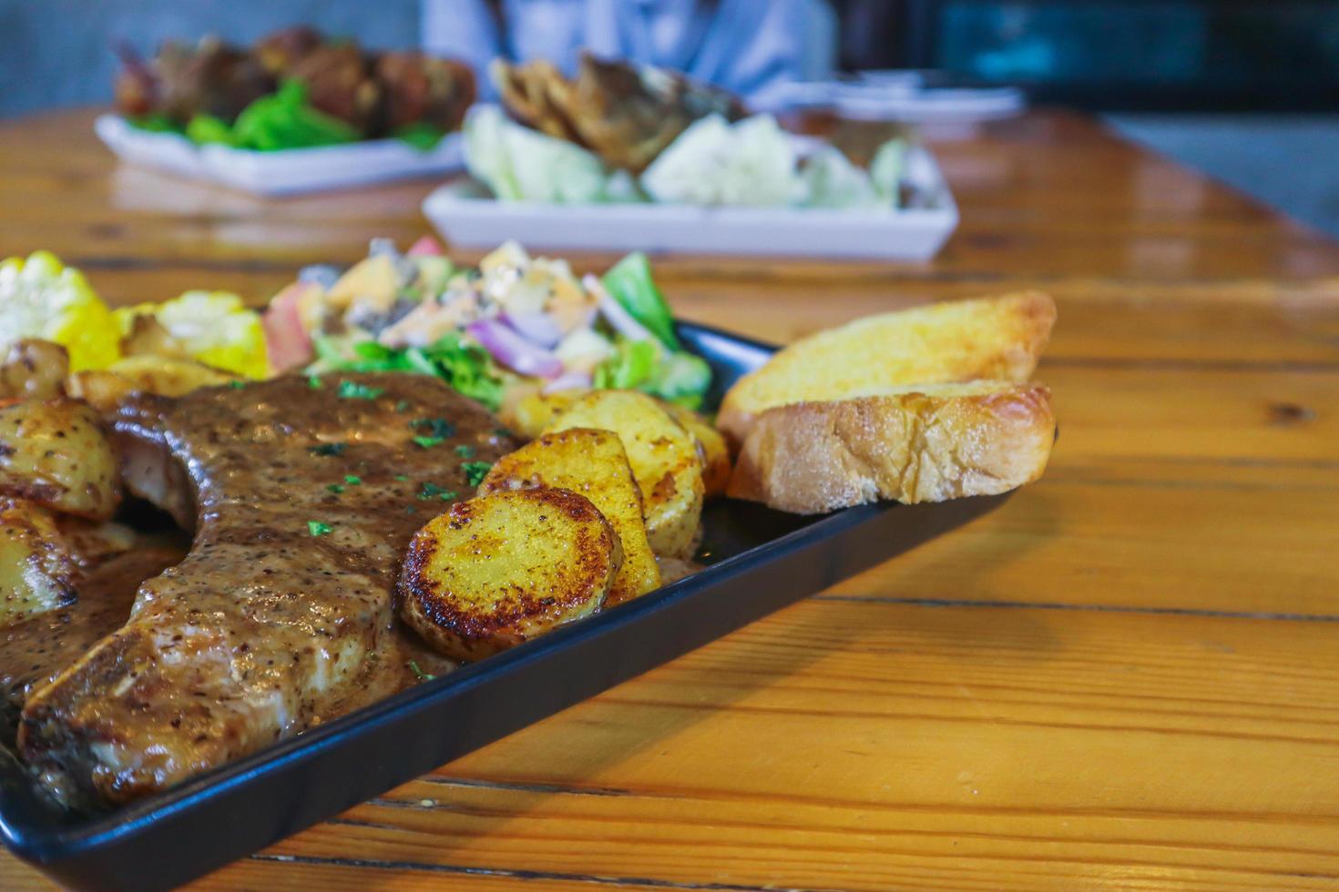 el bistec de ternera a la parrilla con salsa se sirve con una ensalada de frutas y verduras dentro de un plato de cerámica negra en la mesa del comedor para preparar el bistec para una cena festiva. foto