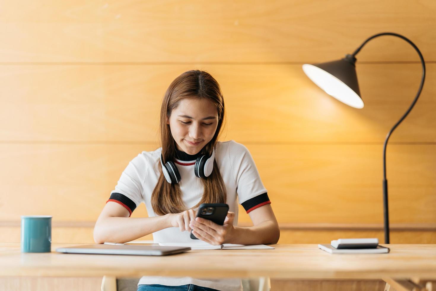 asiático feliz en el uso de auriculares portátil tomar cursos de capacitación en línea tomar notas. una joven estudiante asiática sonriente con auriculares estudia en una computadora desde casa. concepto de educación a distancia. foto