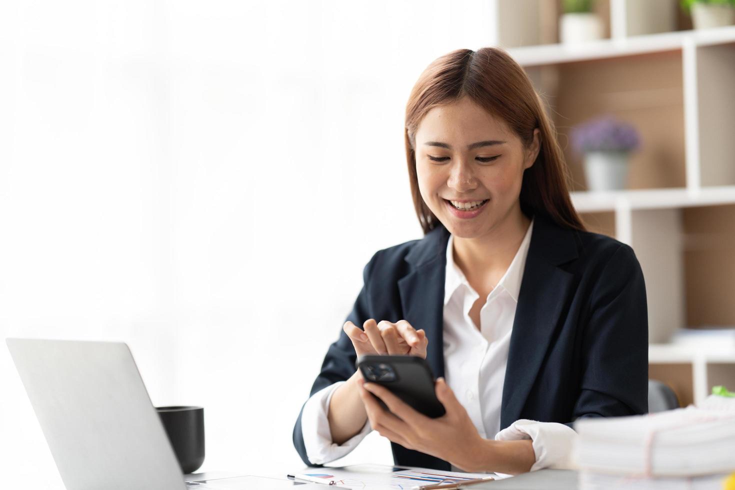 Asian businesswoman in formal suit in office happy and cheerful during using smartphone and working, copy space. photo