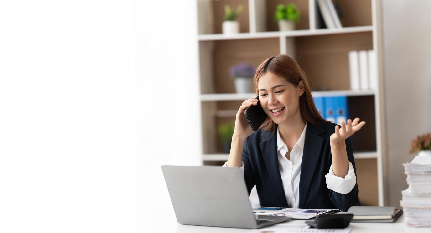 Asian businesswoman in formal suit in office happy and cheerful during using smartphone and working, copy space. photo