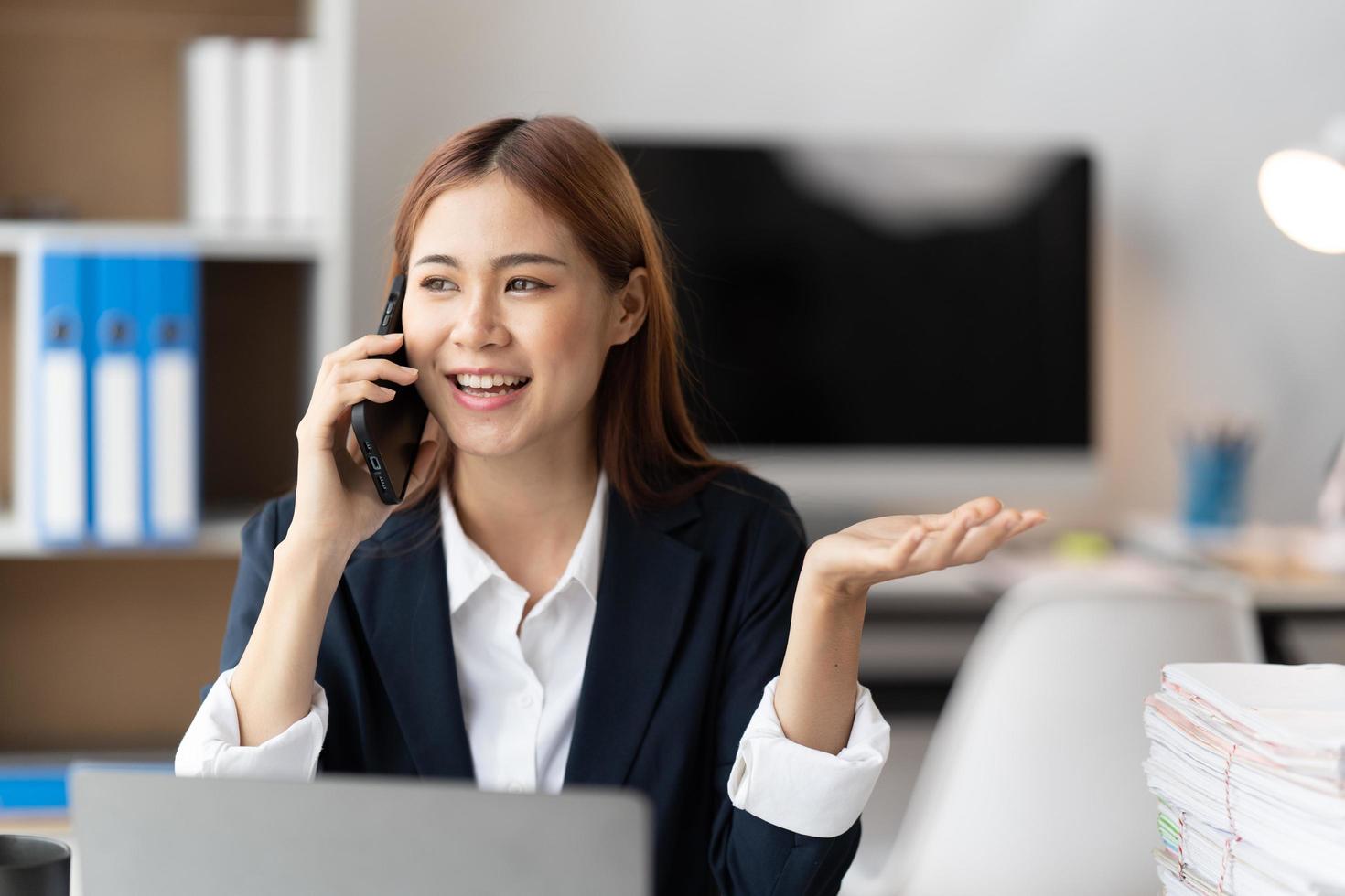 Asian businesswoman in formal suit in office happy and cheerful during using smartphone and working, copy space. photo