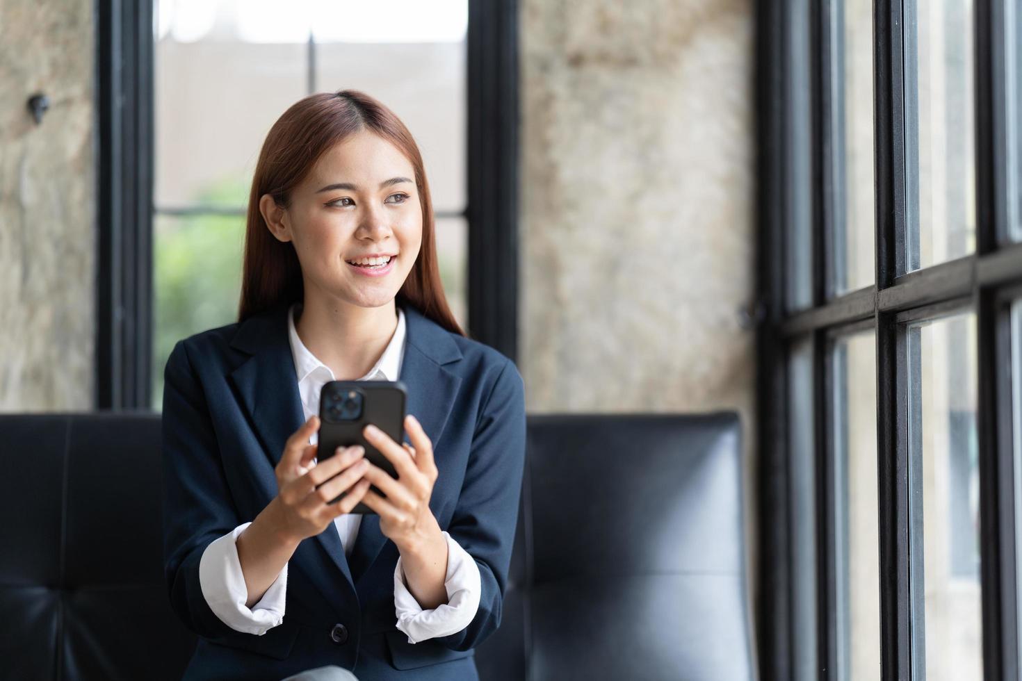 Asian businesswoman in formal suit in office happy and cheerful during using smartphone and working, copy space. photo