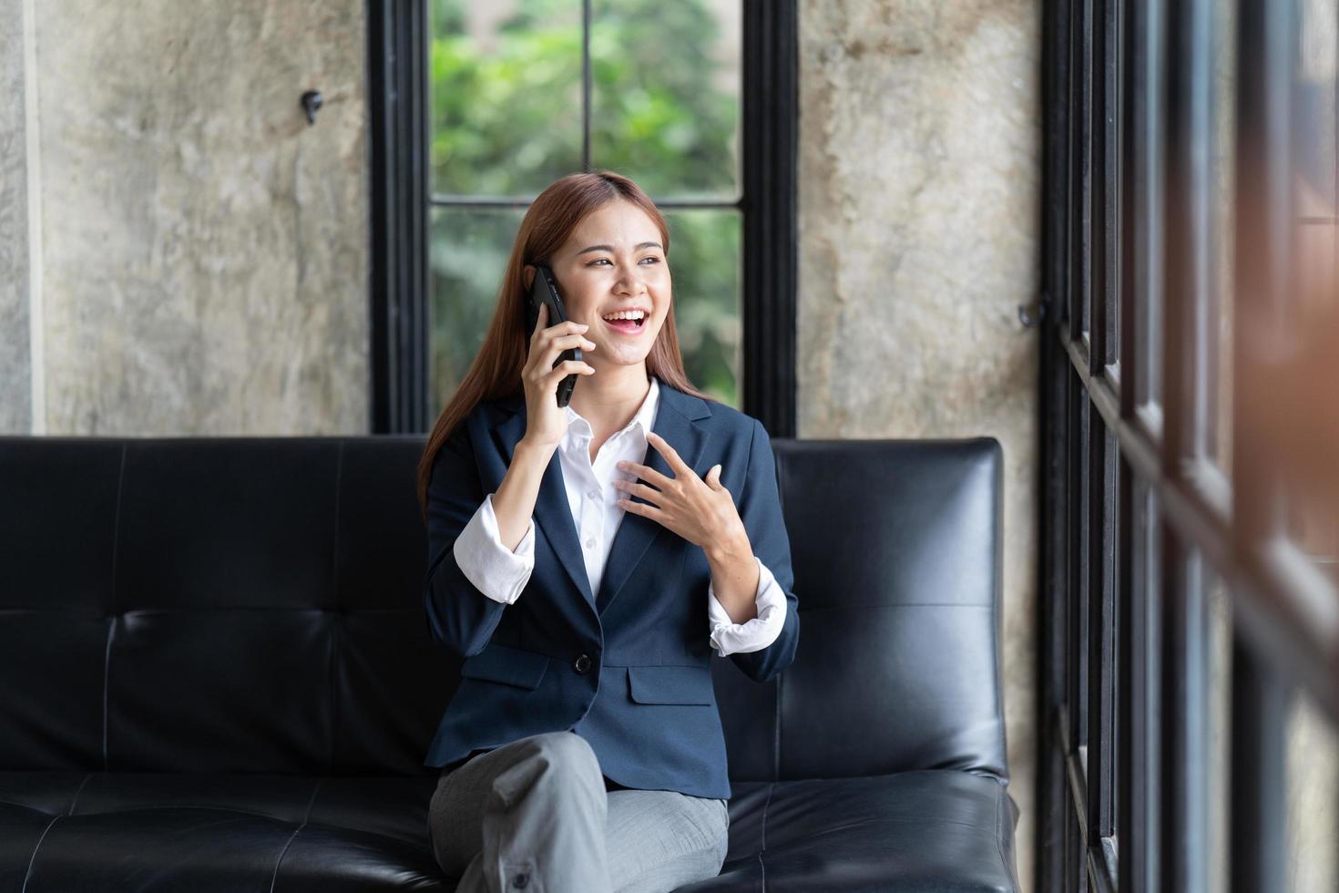 Asian businesswoman in formal suit in office happy and cheerful during using smartphone and working, copy space. photo