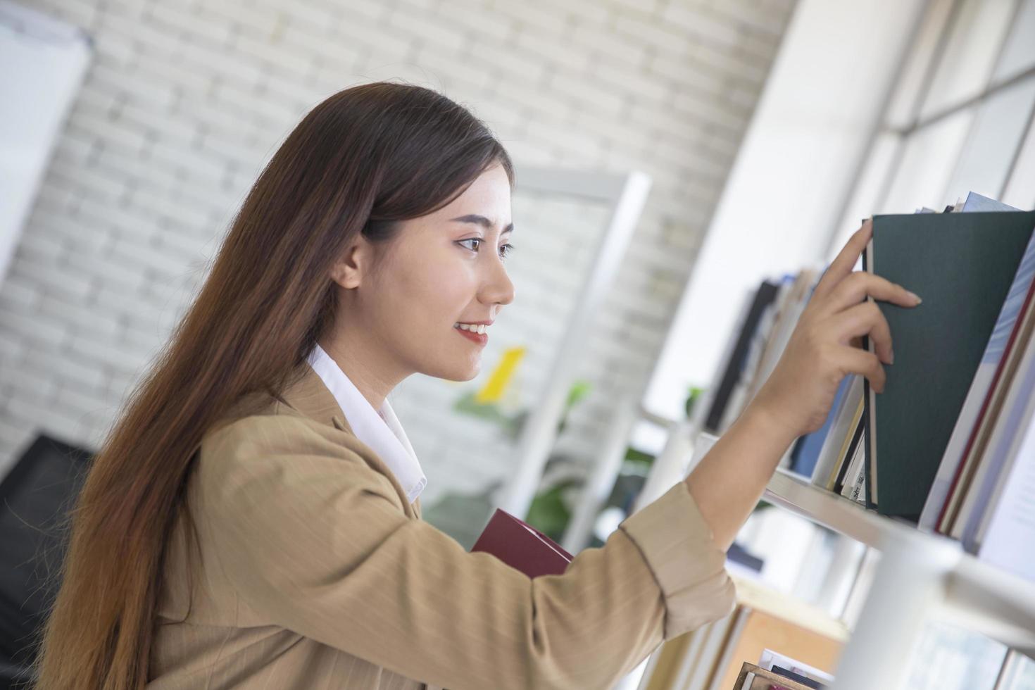 mujer joven tomando libros de búsqueda y tomando un libro en una estantería de biblioteca foto