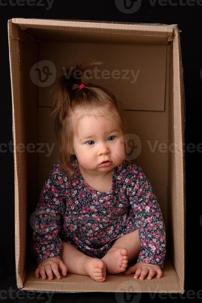 Happy little girl sitting in a cardboard box and having fun photo