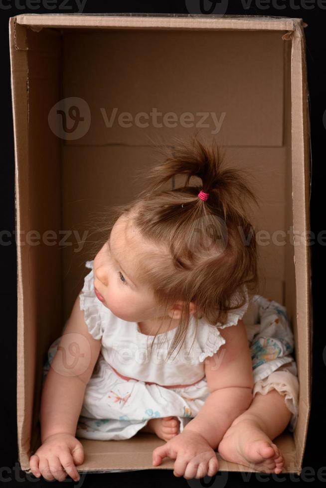 Happy little girl sitting in a cardboard box and having fun photo