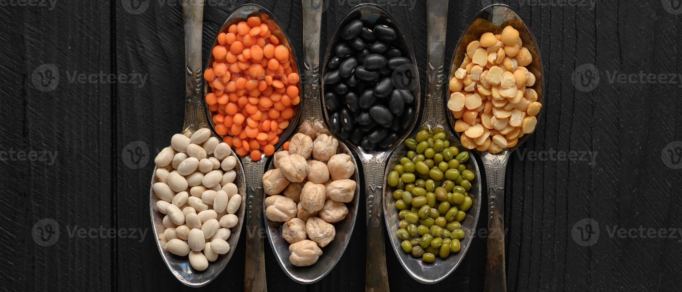 Variety of legumes in old silver spoons on a black wooden background. photo