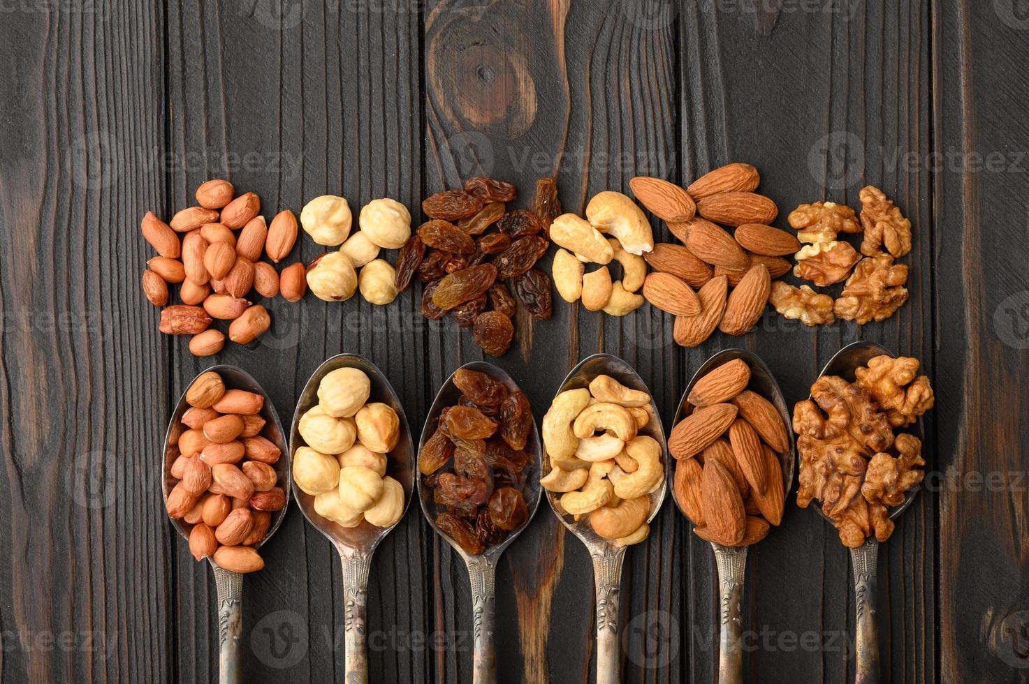 avellanas, anacardos, pasas, almendras, cacahuetes, nueces en cucharas de plata sobre un fondo rústico foto