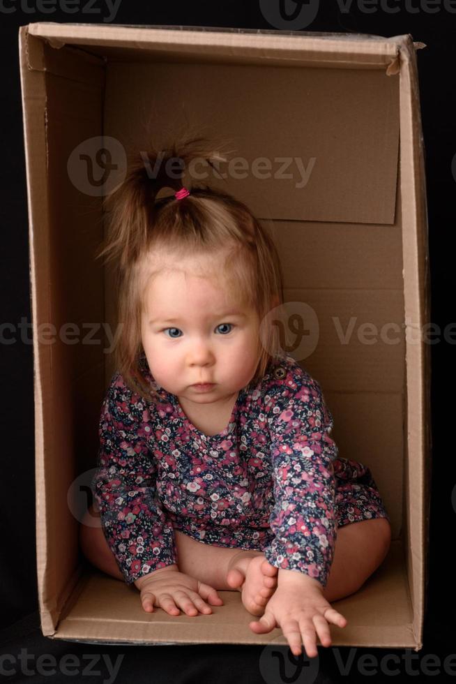 Happy little girl sitting in a cardboard box and having fun photo