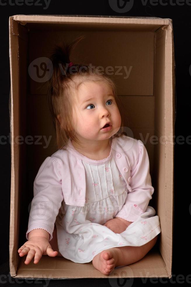 Happy little girl sitting in a cardboard box and having fun photo