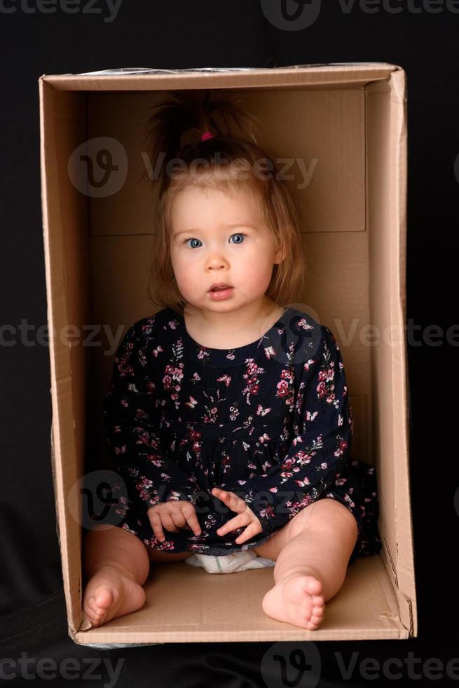 Happy little girl sitting in a cardboard box and having fun photo