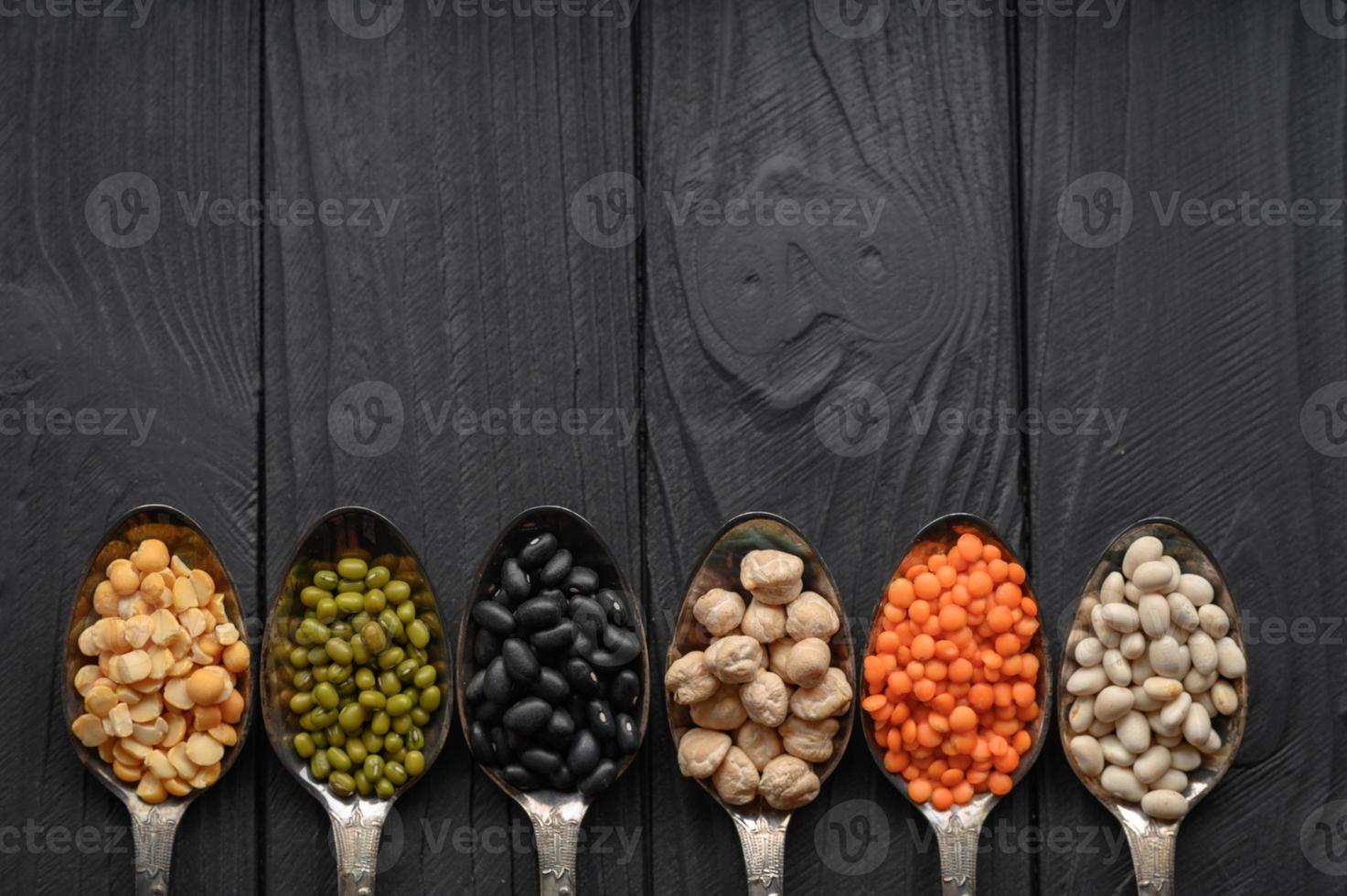 Variety of legumes in old silver spoons on a black wooden background. photo