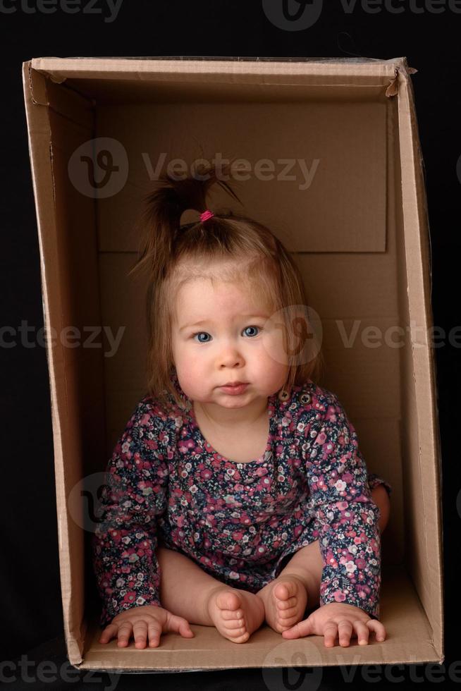 Happy little girl sitting in a cardboard box and having fun photo