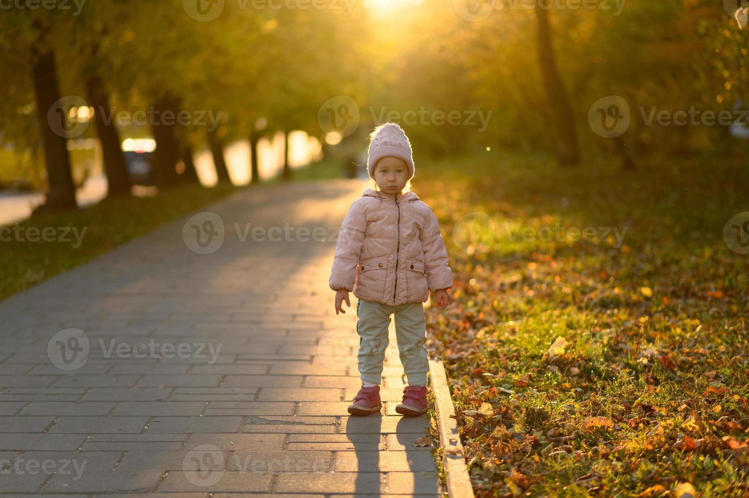 A girl in a pink jacket stands at sunset. photo