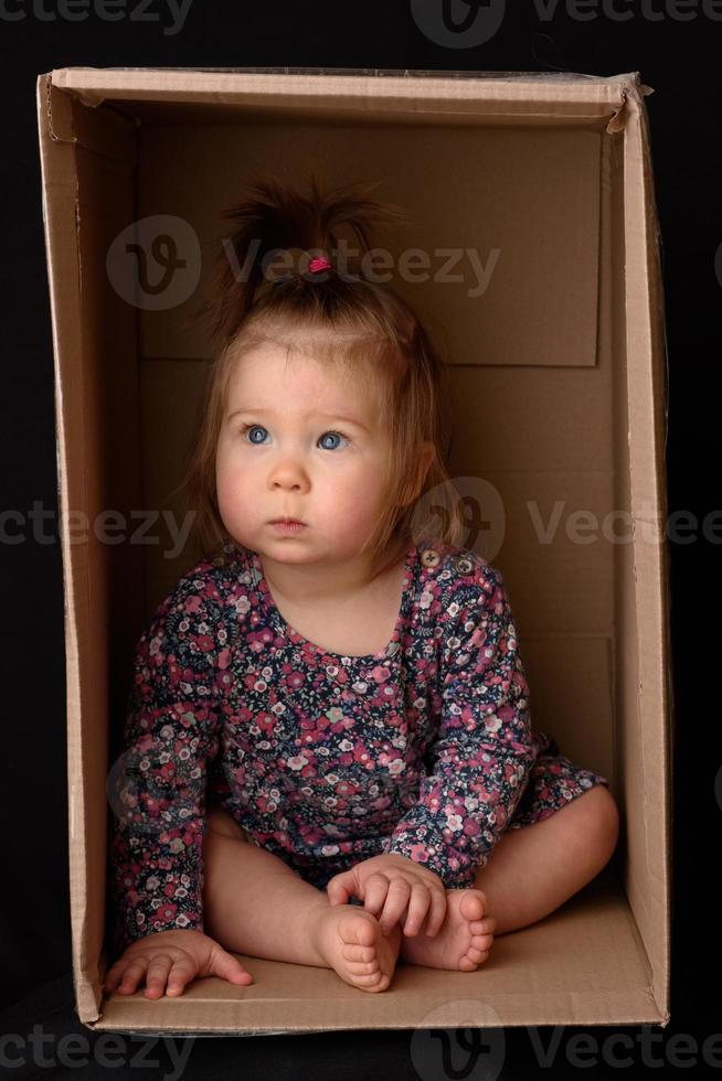 Happy little girl sitting in a cardboard box and having fun photo