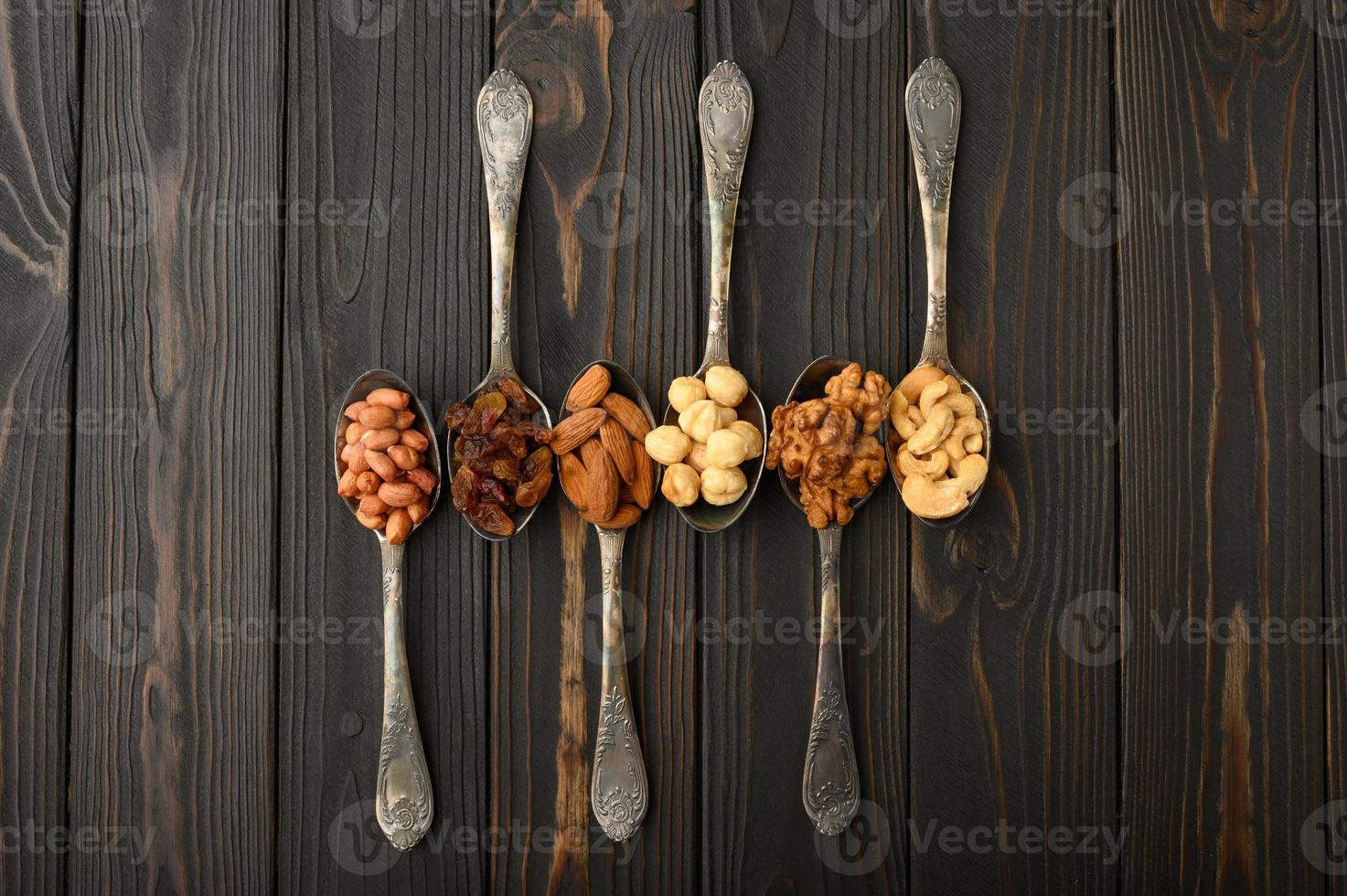 Hazelnut, cashews, raisins, almonds, peanuts, walnuts in silver spoons on a rustic background photo