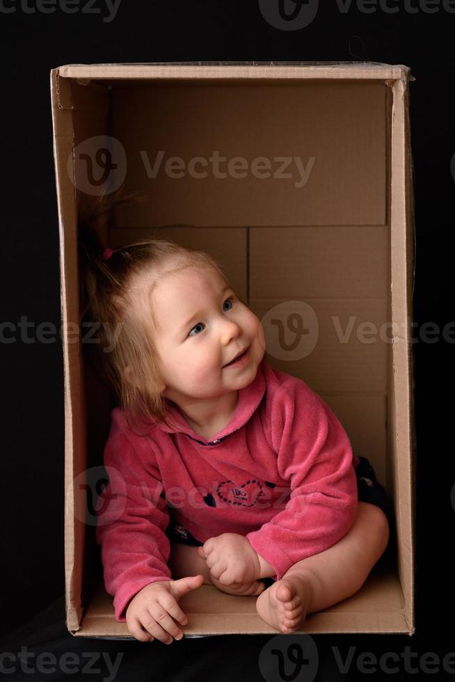 Happy little girl sitting in a cardboard box and having fun photo