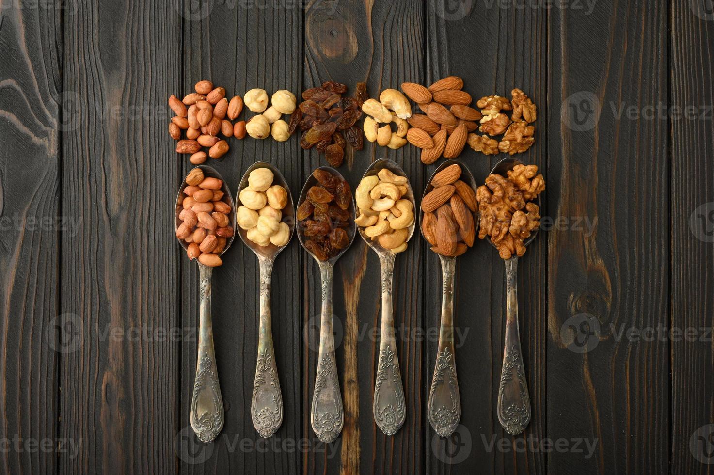 Hazelnut, cashews, raisins, almonds, peanuts, walnuts in silver spoons on a rustic background photo