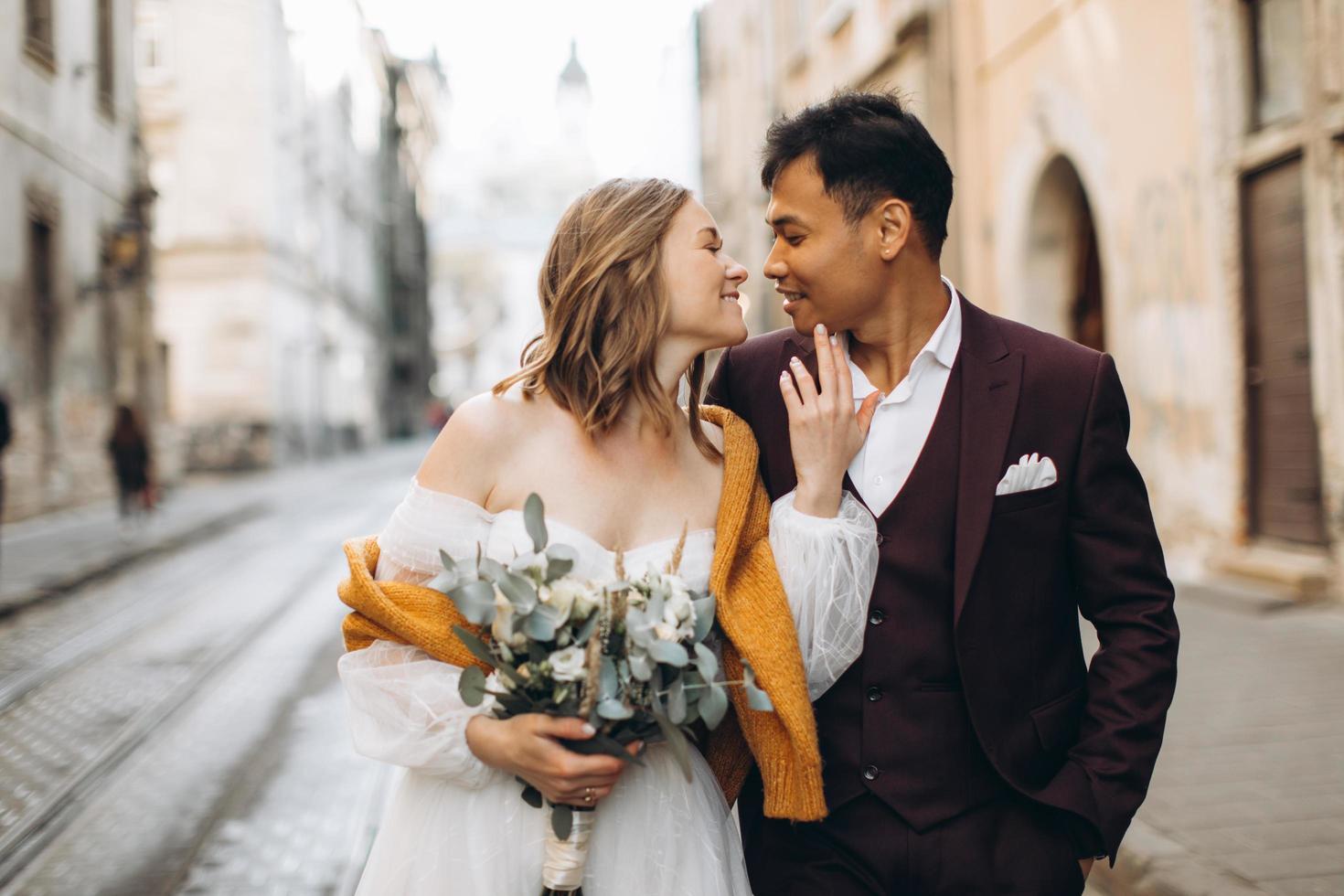 An international wedding couple, a European bride and an Asian groom walk around the city together. photo