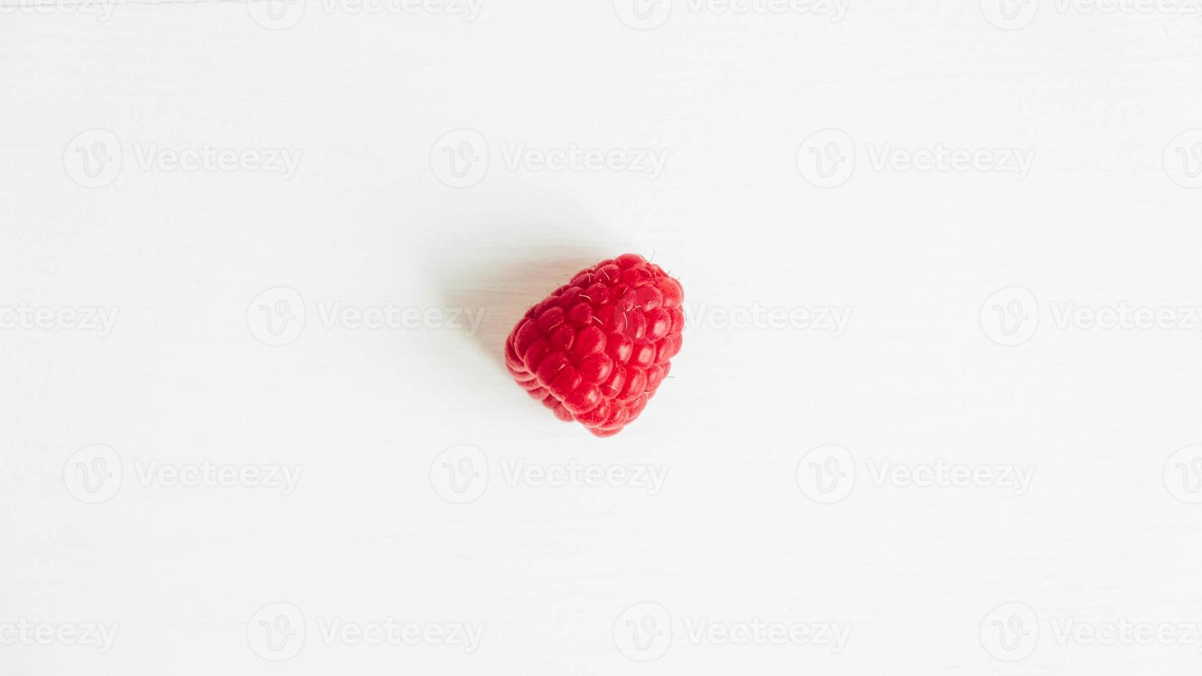 One raspberry lying on a white table background photo