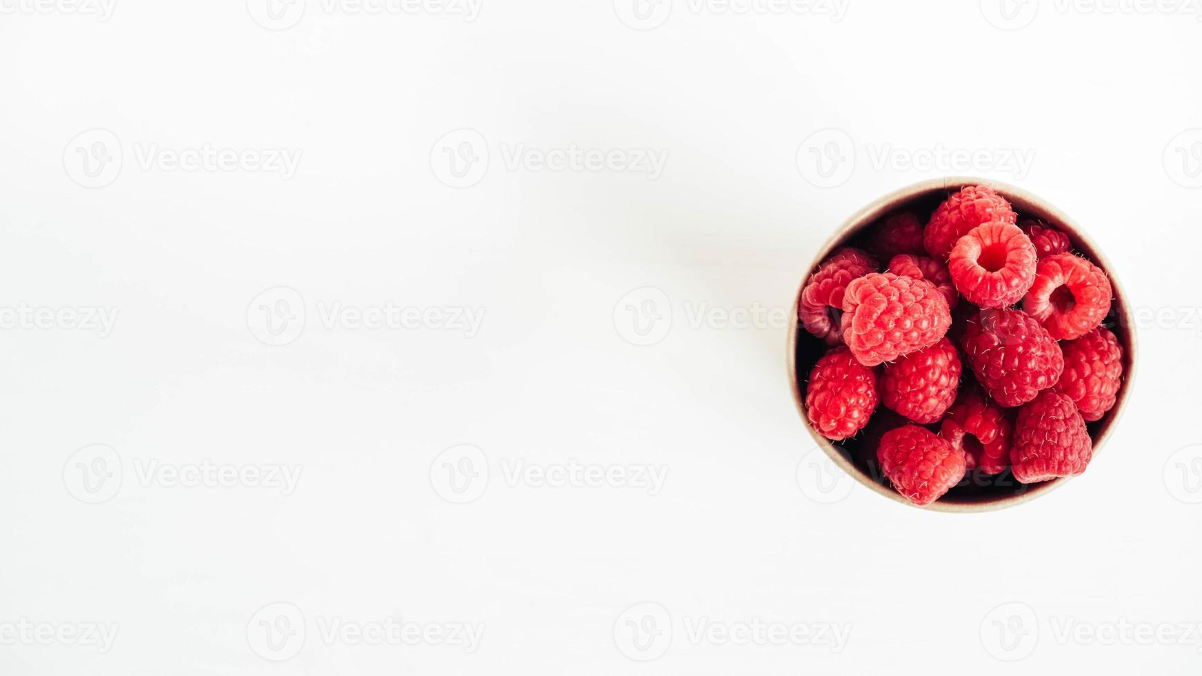 frambuesas rojas frescas en un vaso de papel sobre un fondo de mesa blanco foto