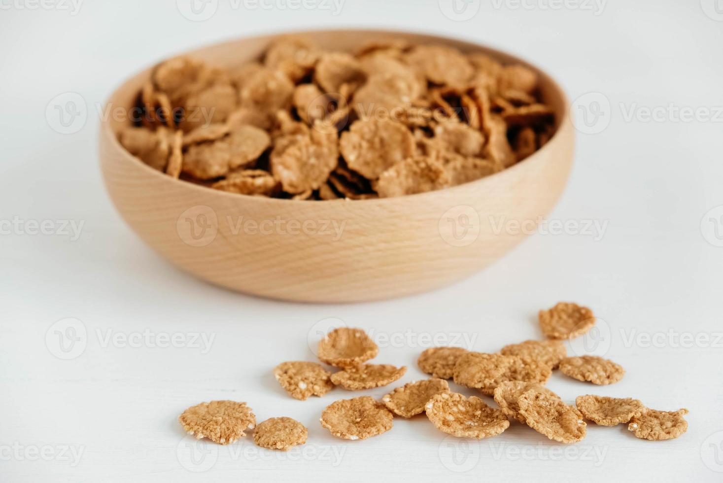 Crispy healthy dry cereal flakes in a wooden bowl on white background photo