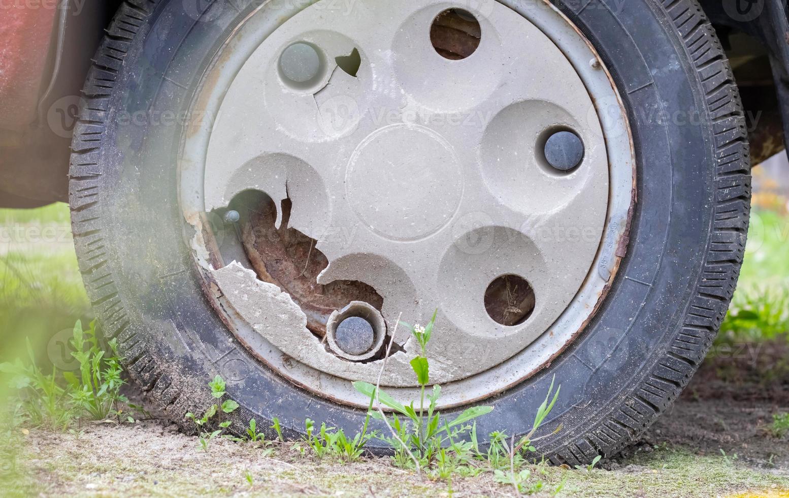 Weathered car wheel with dirt and grime. Rusty abandoned car in the parking lot. Restoration of a retro car. Flat tire. Vintage wheel with classic red car cap. photo
