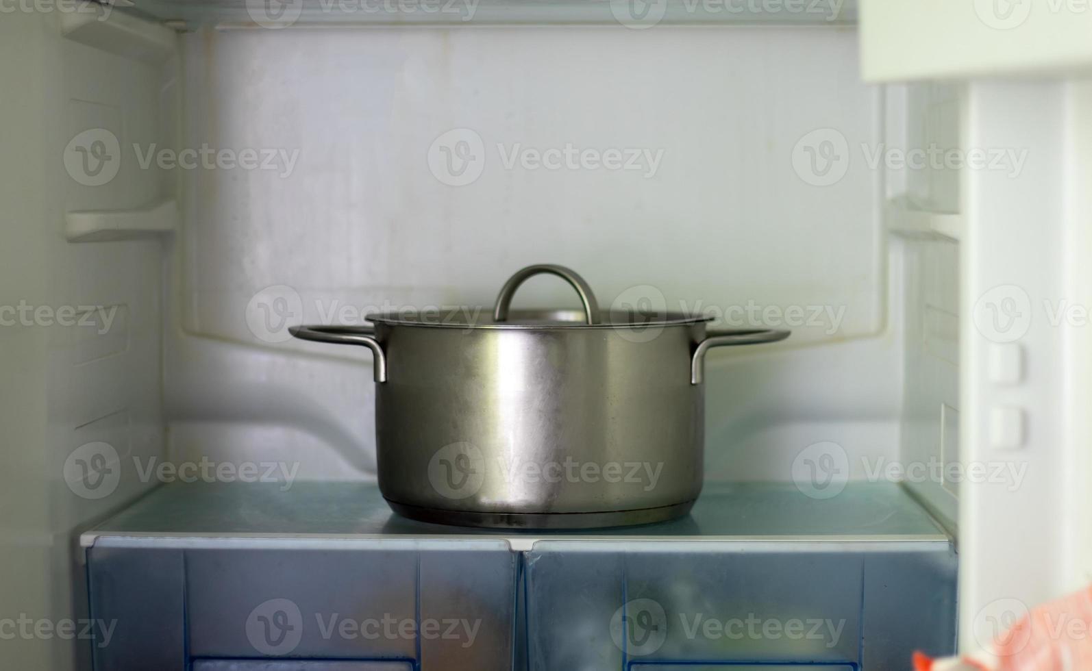 Freezer open pot close-up. Saucepan in an open refrigerator. The refrigerator inside is almost empty due to the economic crisis. Open refrigerator shelves with various cooked food. photo