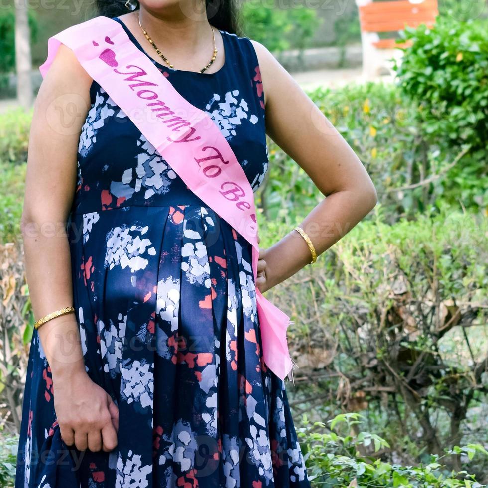 Indian couple posing for maternity baby shoot. The couple is posing in a lawn with green grass and the woman is falunting her baby bump in Lodhi Garden in New Delhi, India photo