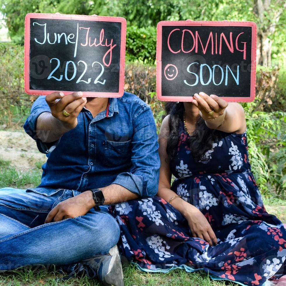 Indian couple posing for maternity baby shoot. The couple is posing in a lawn with green grass and the woman is falunting her baby bump in Lodhi Garden in New Delhi, India photo