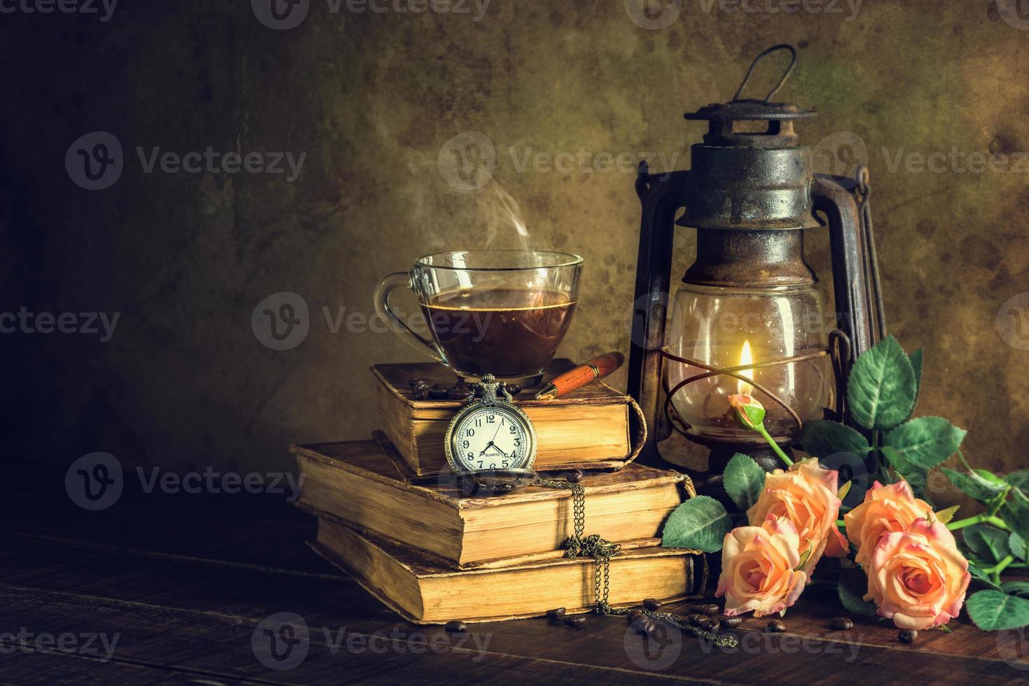 Coffee in cup glass on old books and clock vintage with kerosene lamp oil lantern burning with glow soft light on aged wood floor. photo