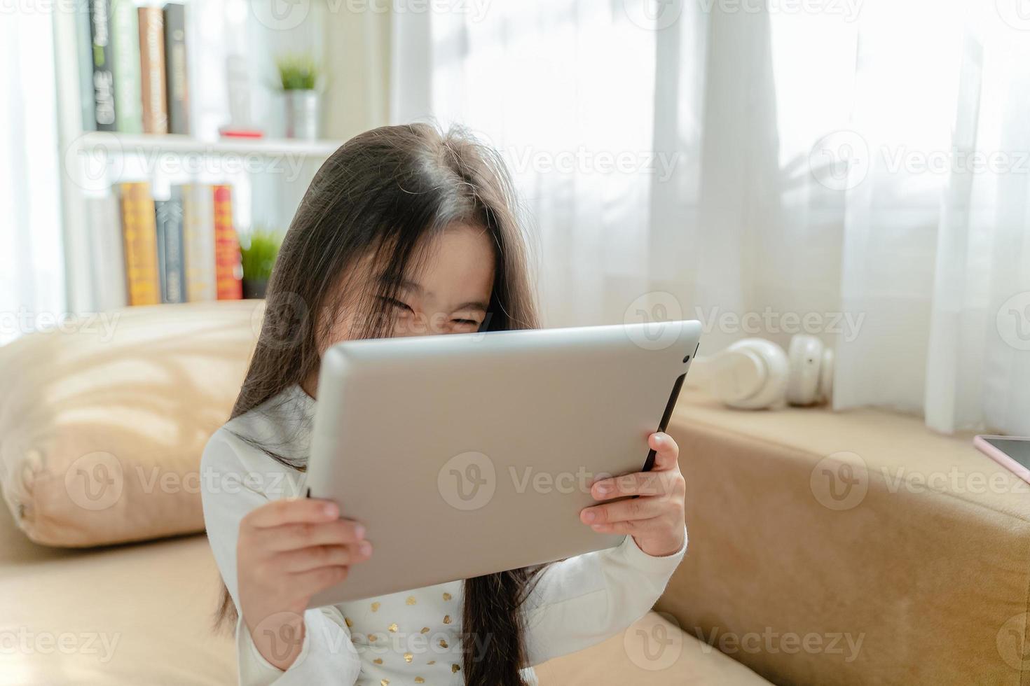 Cute child using a tablet  and smiling while sitting on sofa at home photo