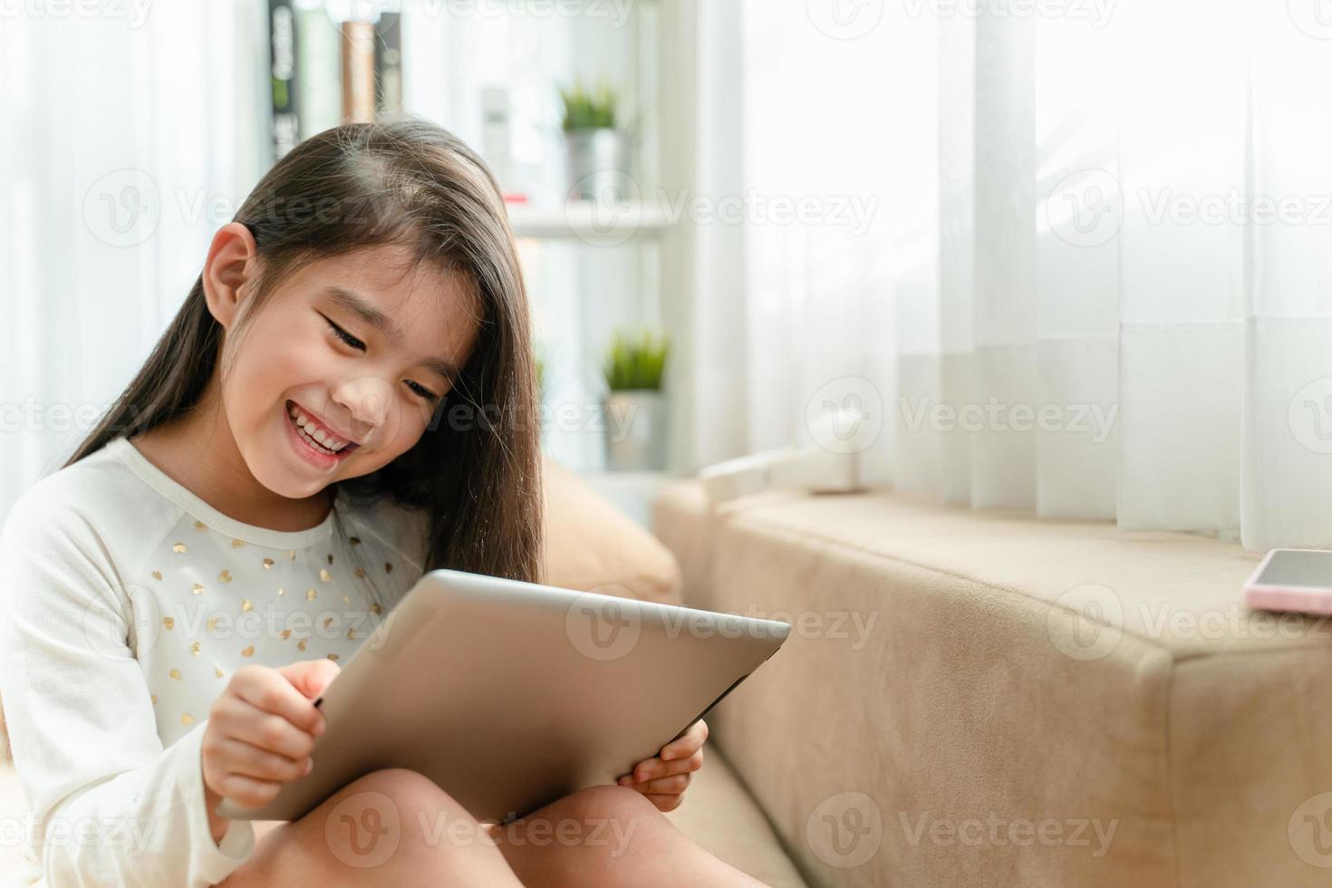 Cute child using a smartphone and smiling while sitting on sofa at home photo