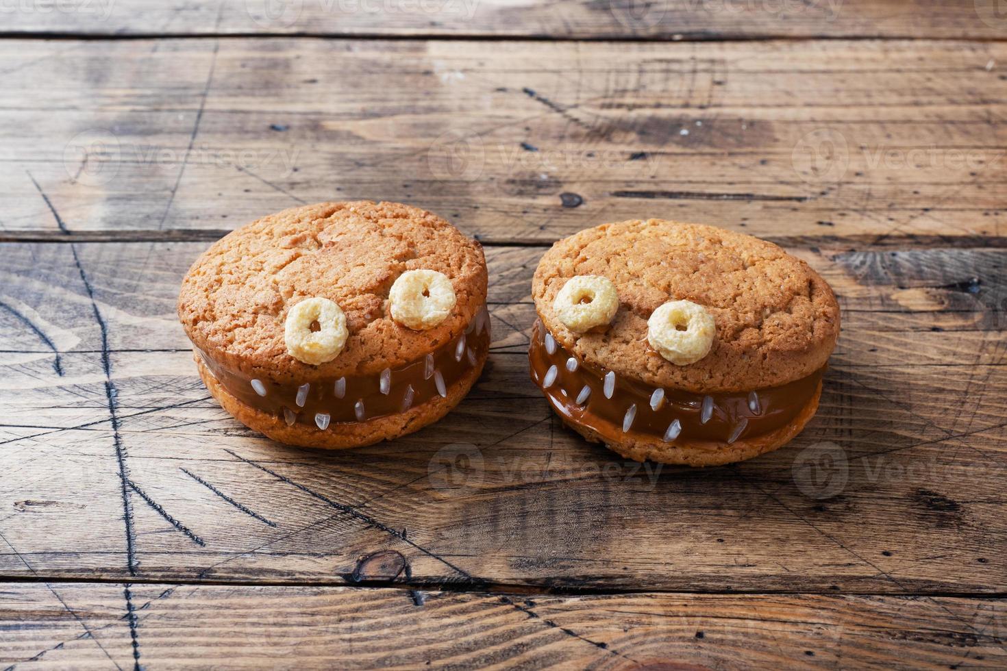 Cookies with cream paste in the shape of monsters for Halloween celebration. Funny homemade faces made of oatmeal cookies and boiled condensed milk. copy space photo