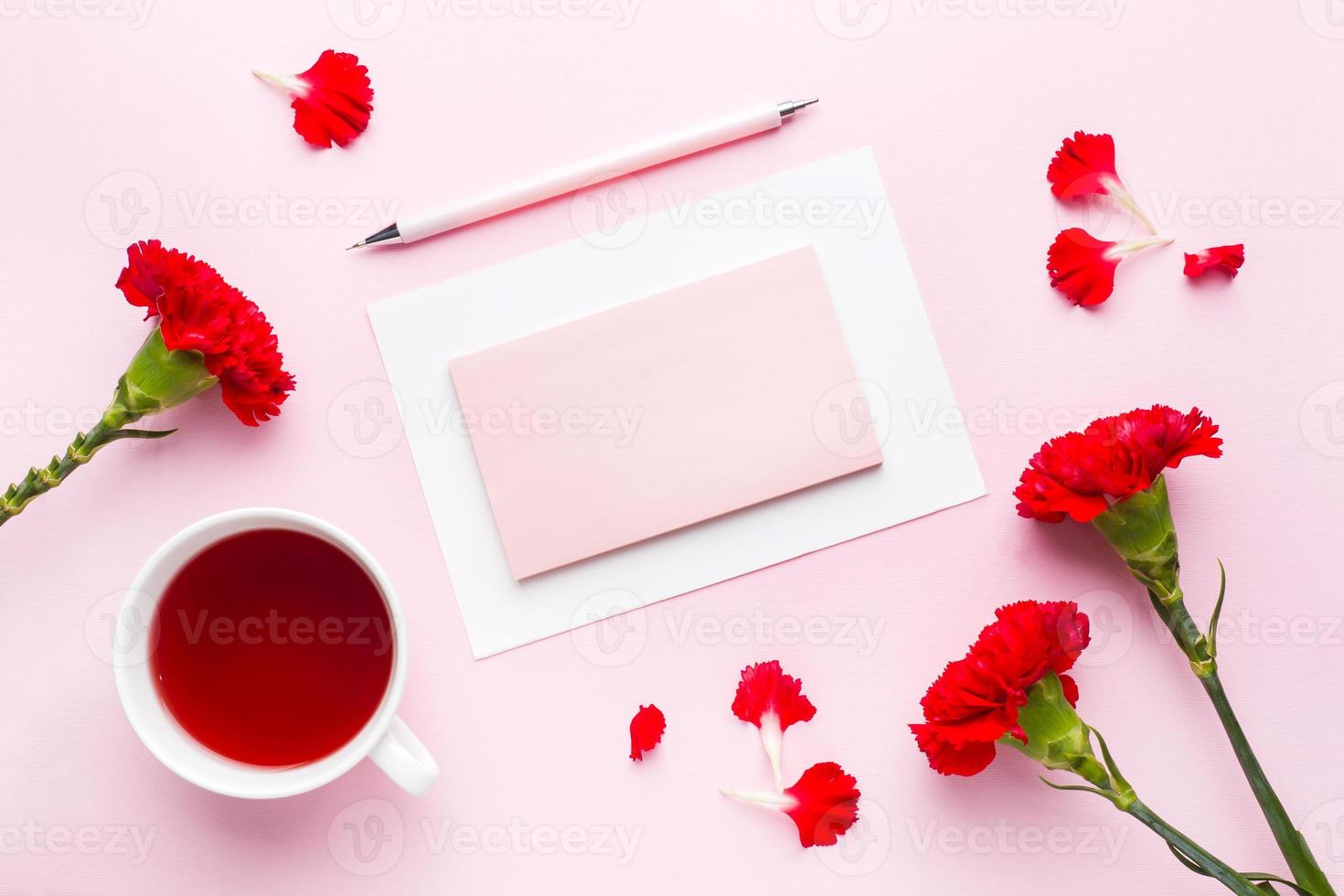 Red-pink objects. Cup of tea, carnation flowers Notepad for text on pastel pink background. Copy space. Top view Flat lay photo