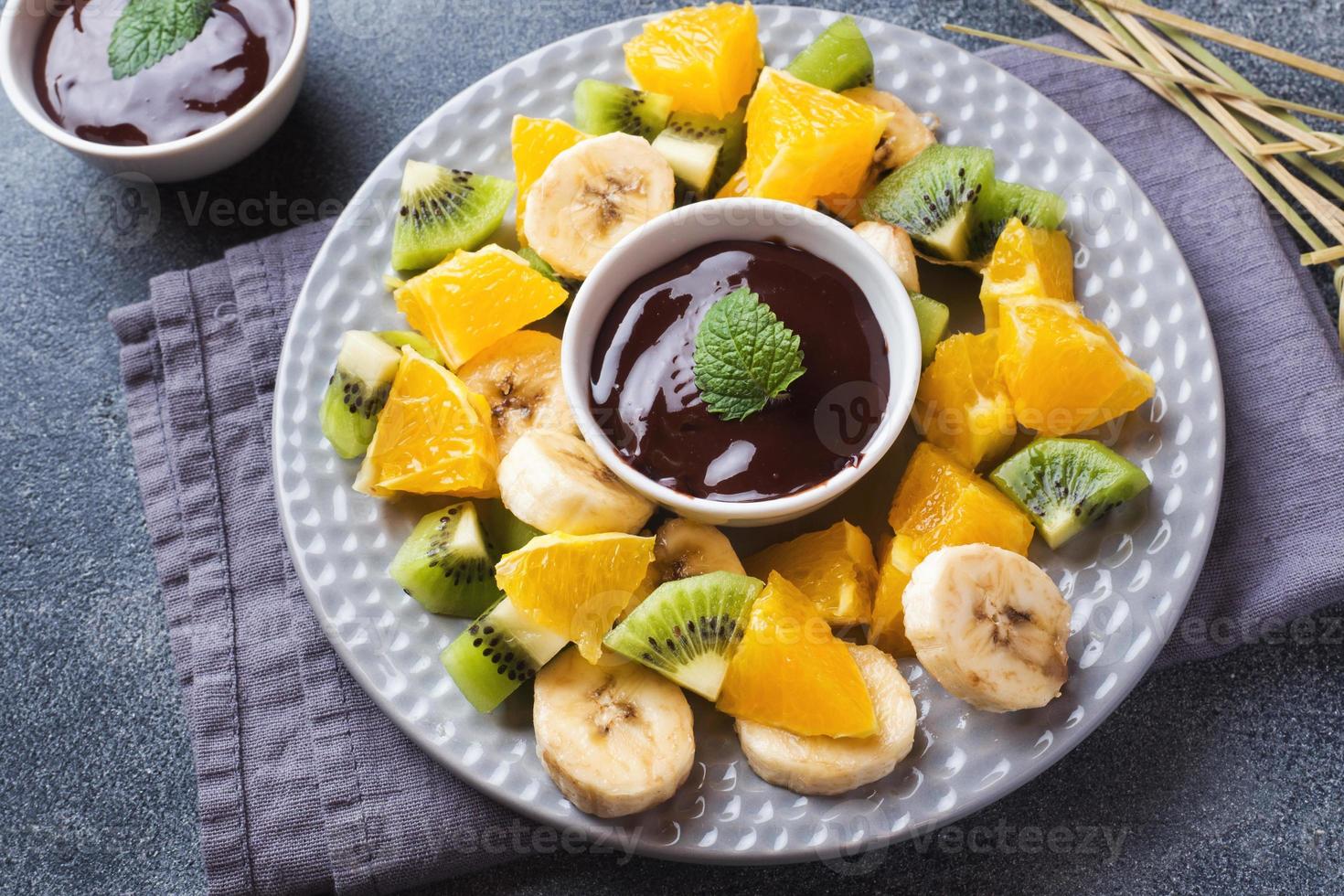 fondue de chocolate con frutas sobre un fondo de hormigón oscuro. concepto de fiesta de verano. copie el espacio foto