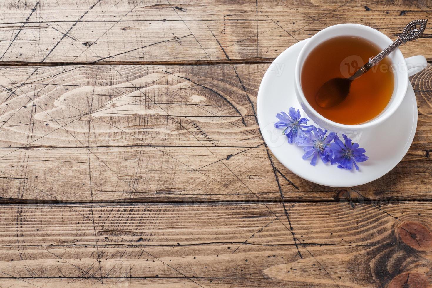 Cup with chicory drink and blue chicory flowers on wooden table. Copy space. photo