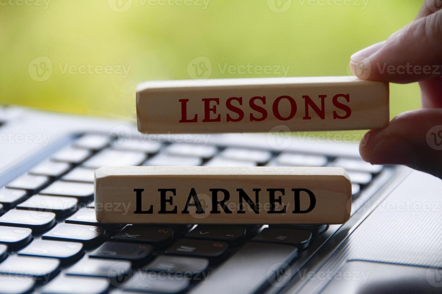 Hand holding lessons learned text on wooden blocks on top of a laptop with blurred nature background. Learning concept photo