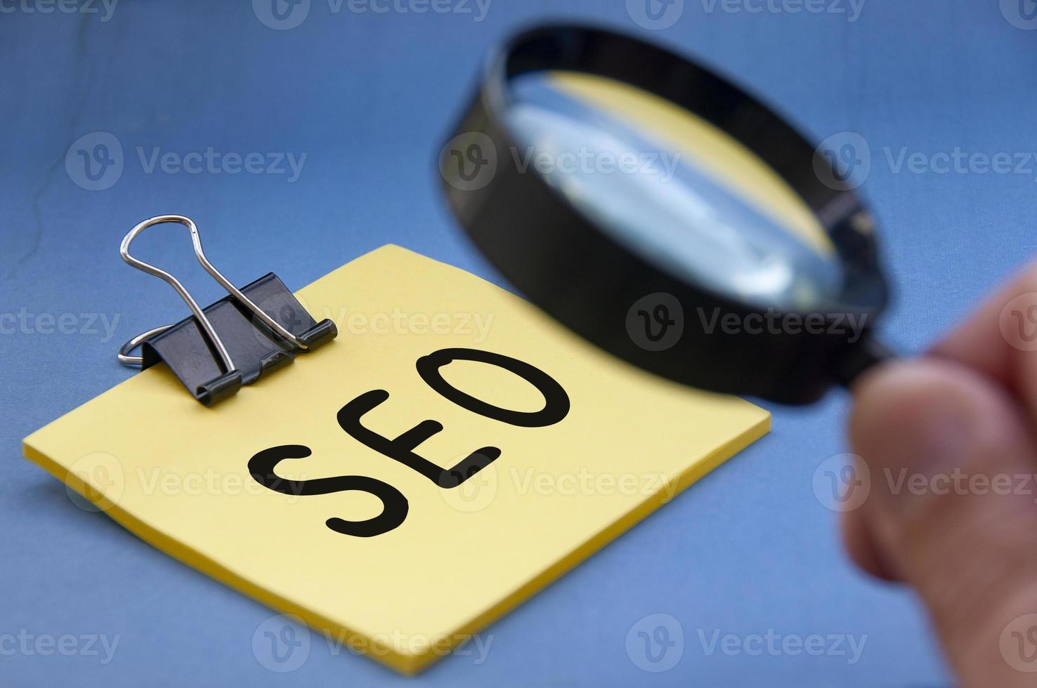 Search Engine Optimization text on sticky note with hand holding magnifying glass. Online business and affiliate marketing concept photo