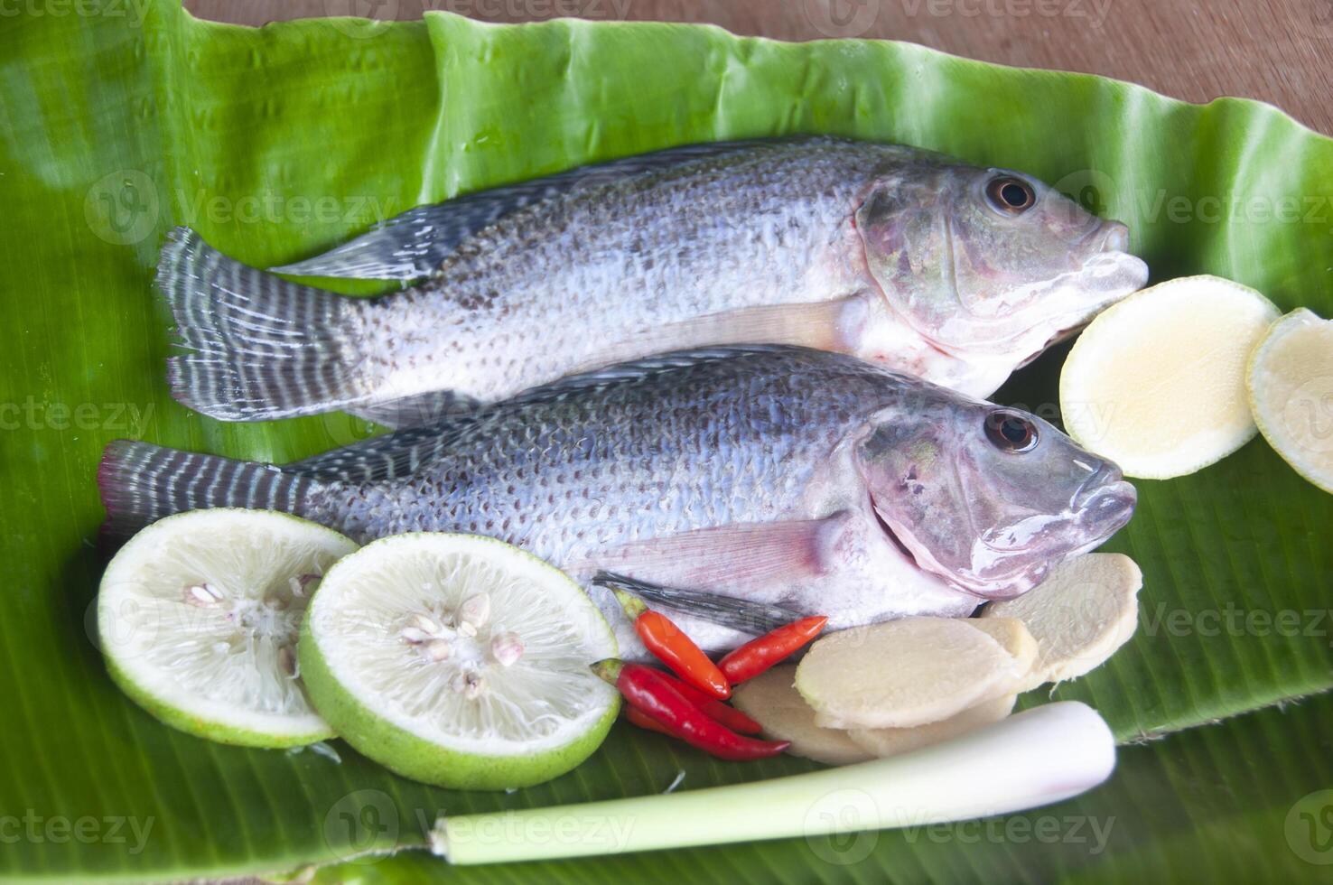 Fresh tilapia fish with lemongrass, lemon and chili on banana leaf. photo