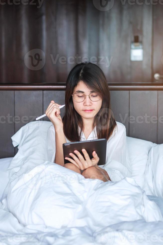 Happy woman using tablet for social media, young female watching movies on computer pad on bed at home. technology, network, online shopping, e commerce, lifestyle and digital communication concept photo