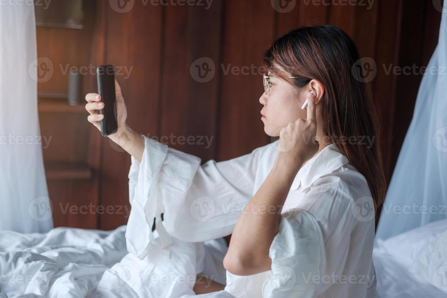 Happy woman using smart phone for video call, female meeting  online by mobile phone on bed. technology, network, work from home, lifestyle and digital communication concept photo