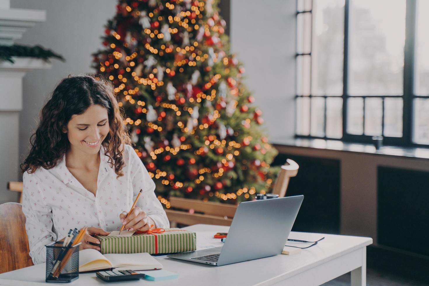 Pleased european woman office worker writing christmas letter, greeting card with holiday wishes photo