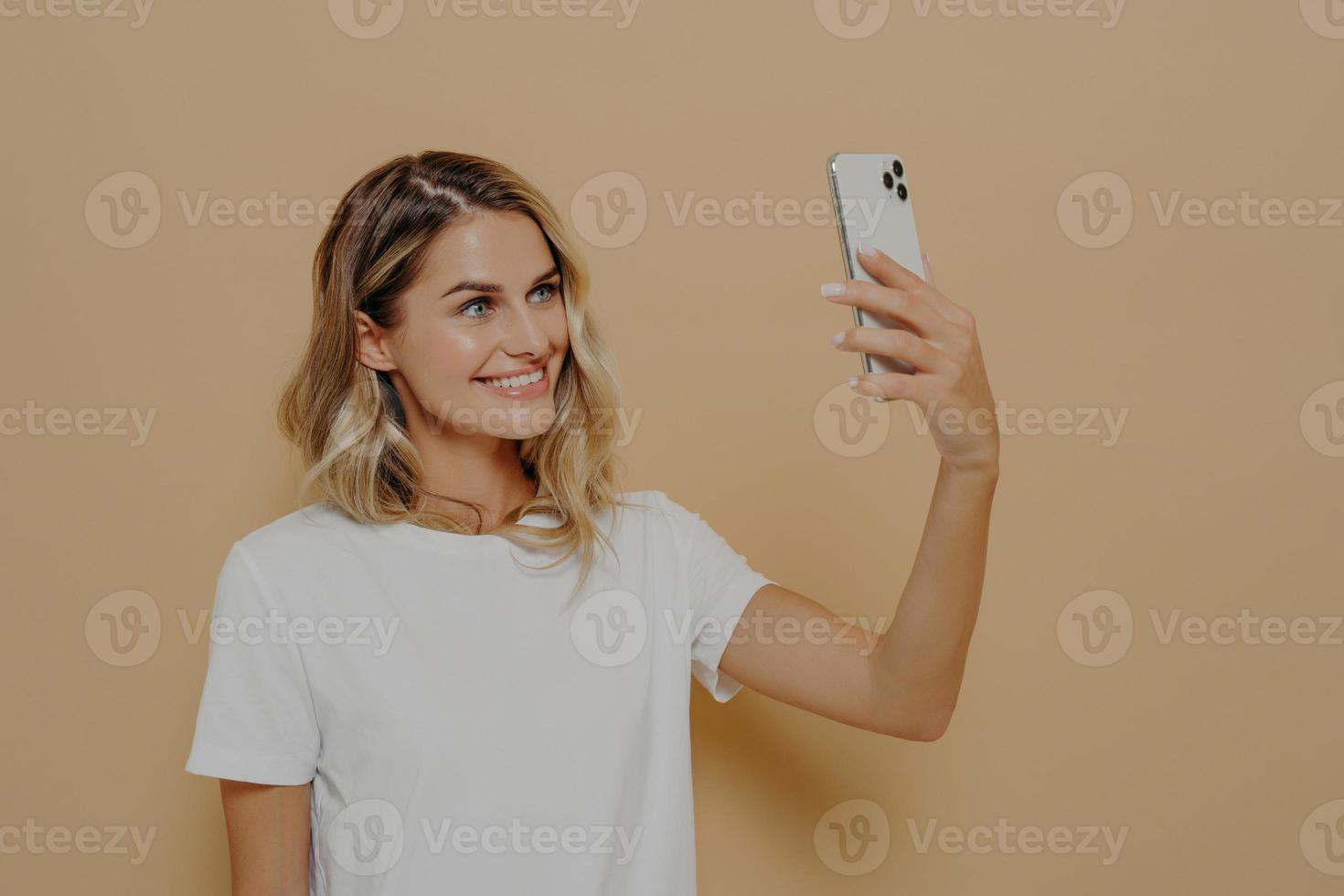 Young blonde smiling woman using smartphone while having video call with family or friend photo