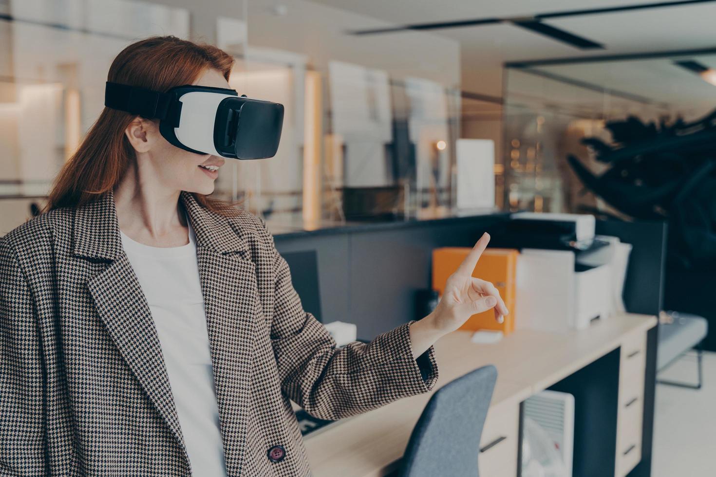 Smiling happy businesswoman wearing VR headset trying out virtual reality for first time at work photo