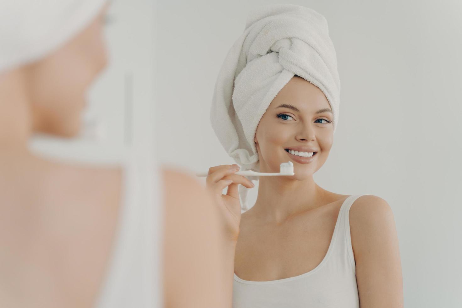 hermosa mujer joven con una sonrisa perfecta y saludable cepillarse los dientes y mirarse en el espejo foto