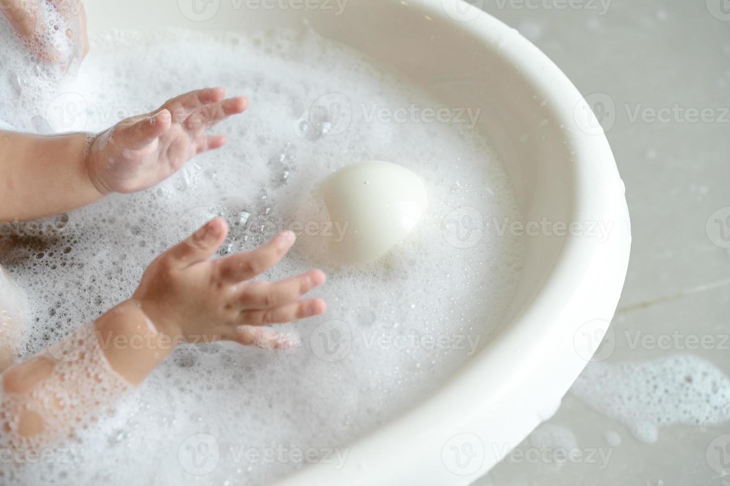 close up baby girl plays bubble in the water while bathing photo