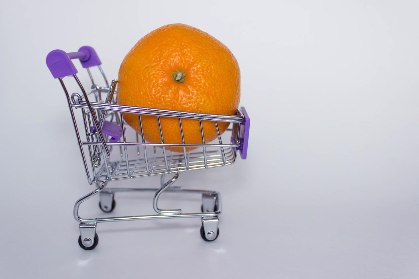 Mini decorative shopping cart with big orange tangerine on white background. With copy space photo