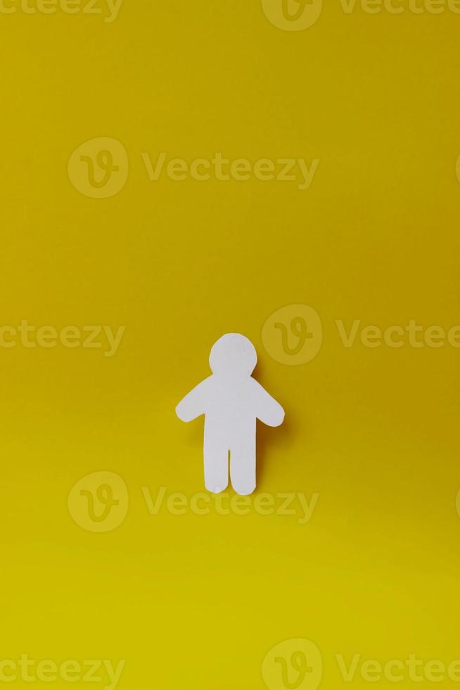 Silhouette of a man of white paper, cut by hand on yellow background. Vertical photo with copy space