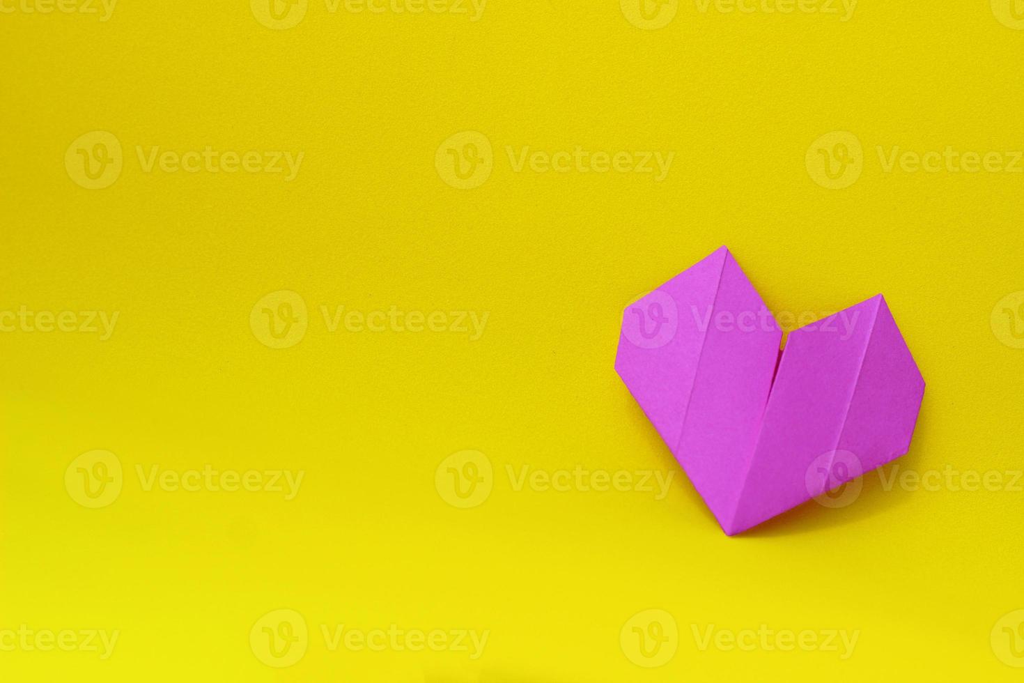 corazón de origami de papel púrpura sobre un fondo amarillo en el lado derecho de la foto. fondo minimalista con espacio de copia foto